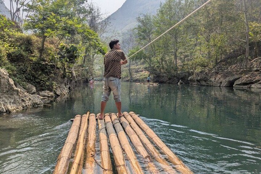 A person standing on a bamboo raft in a river surrounded by trees and mountains. 5