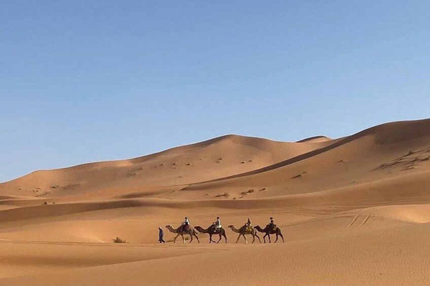 A desert landscape with sand dunes and a group of people riding camels. 2
