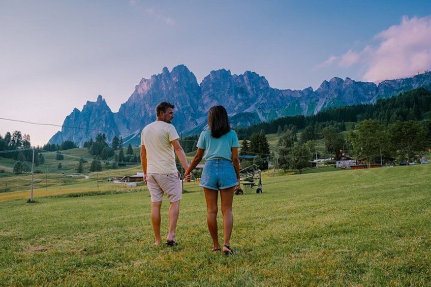 Deux personnes se tenant la main dans un champ herbeux, avec une chaîne de montagnes en arrière-plan. 1