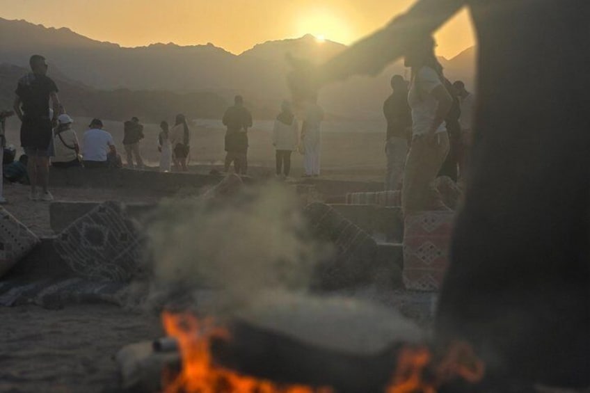 A sunset over a mountainous landscape with people gathered around a fire. 4