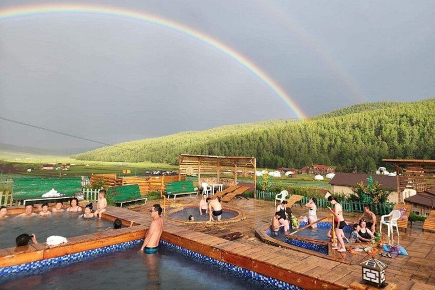 A swimming pool with people, a rainbow, and a forested hill in the background. 3