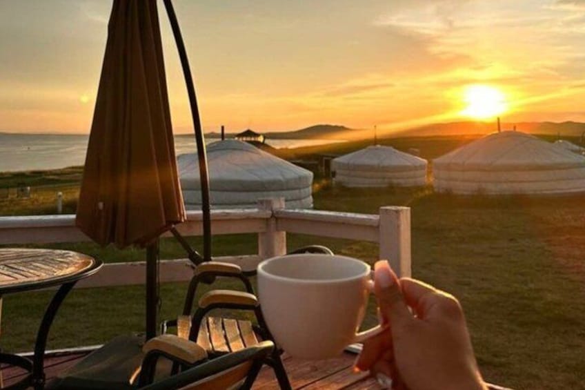 A sunset view with yurts and a person holding a cup. 4