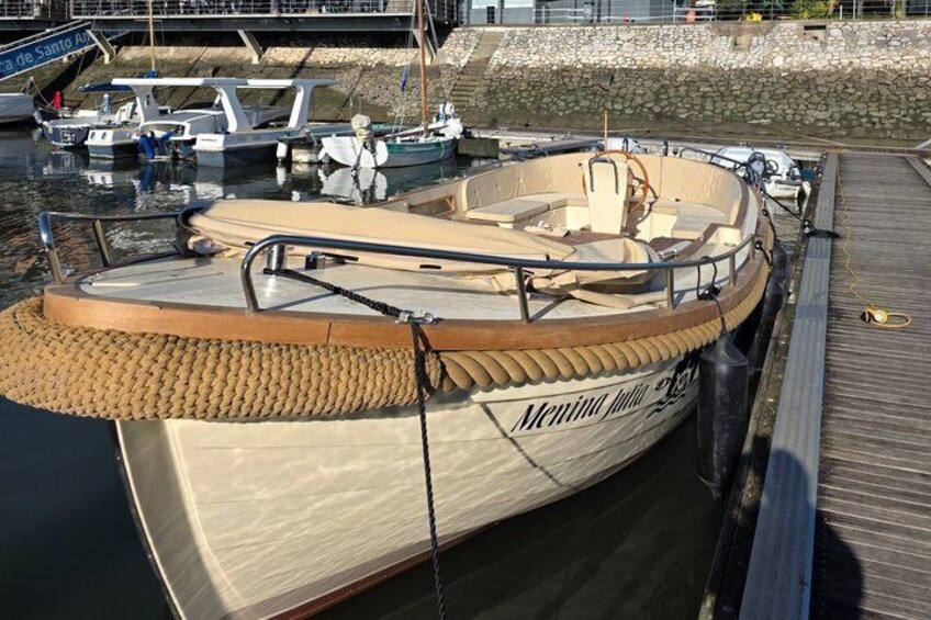 Ein kleines Motorboot namens 'Meningo' liegt in einer Marina festgemacht, im Hintergrund sind weitere Boote zu sehen. 3