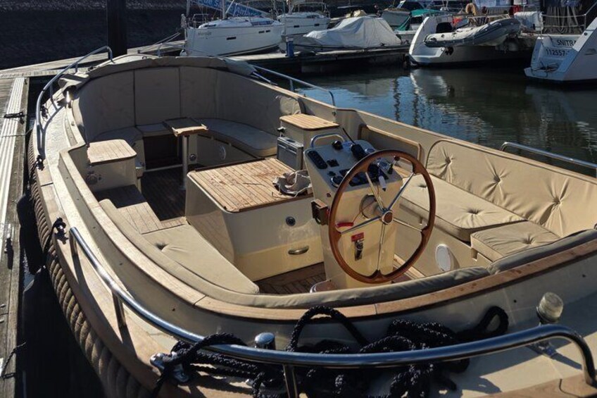 Ein kleines Boot mit Steuer, gepolsterten Sitzen und einem Holzboden. 4