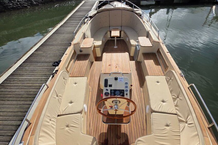 Ein Bootsdeck mit gepolsterten Sitzgelegenheiten, einem zentralen Tisch und einem Steuerrad. 2