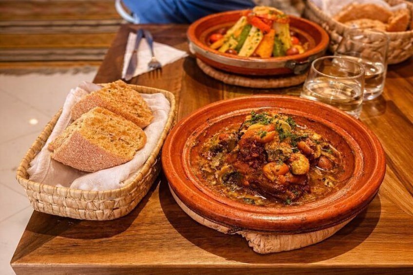 Un plat traditionnel marocain, un tajine, servi avec du pain et des légumes sur une table en bois. 4