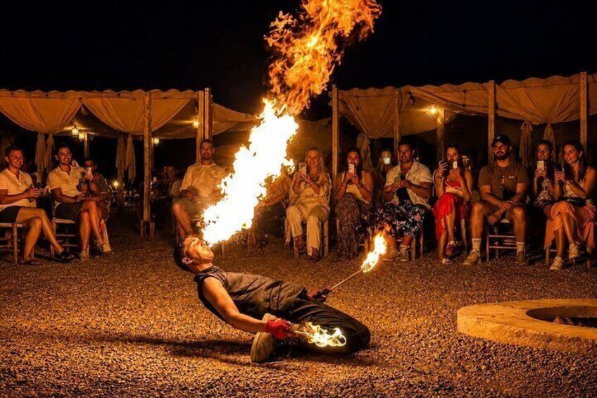 Une personne qui réalise un numéro de jonglage avec le feu, assise par terre, entourée de spectateurs. 4