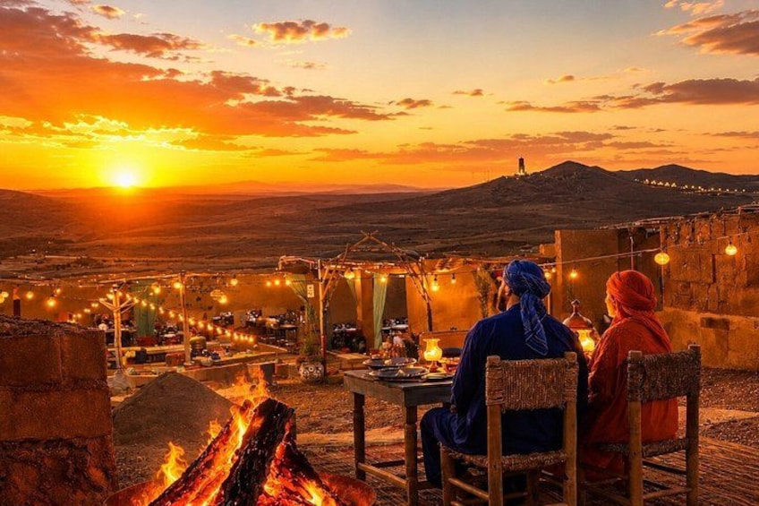 A sunset over a desert landscape with a campfire and string lights. 5
