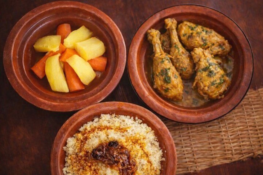 Trois bols en argile contenant des aliments : un bol avec des légumes coupés en tranches, un autre avec du poulet et un troisième avec du couscous. 5