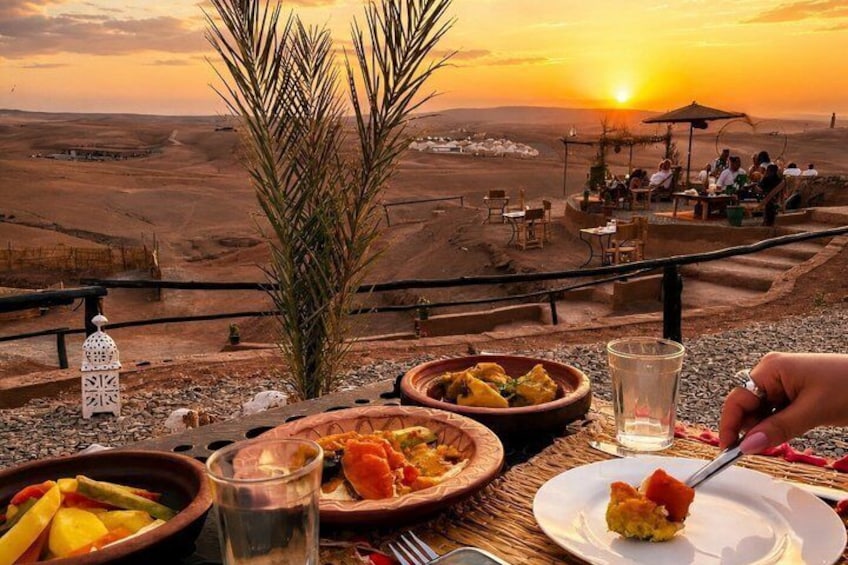 Un paysage désertique au coucher du soleil, une table dressée avec de la nourriture et des personnes qui dînent. 5