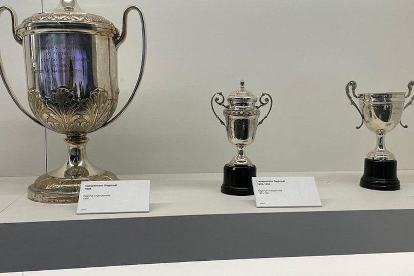 Tres trofeos plateados exhibidos con etiquetas. 3