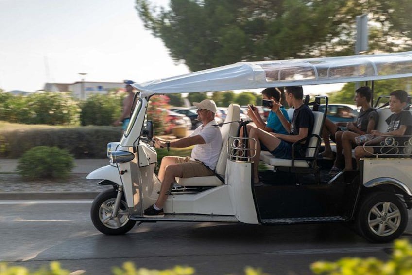 Een golfkar met passagiers, geparkeerd op een straat met groen op de achtergrond. 4