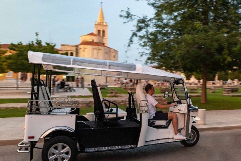 Une voiturette de golf circule sur une route, avec une église en arrière-plan. 4