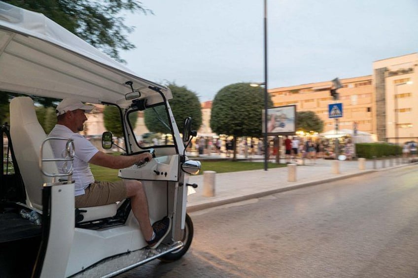 Een man rijdt in een golfkarretje over een stadsweg. 2