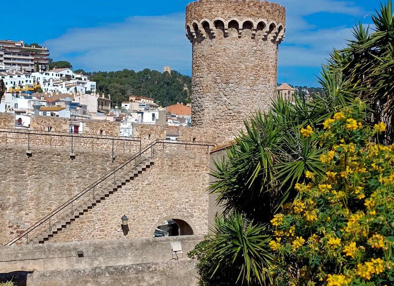 A stone tower with a staircase leading up to it, surrounded by buildings and greenery. 4