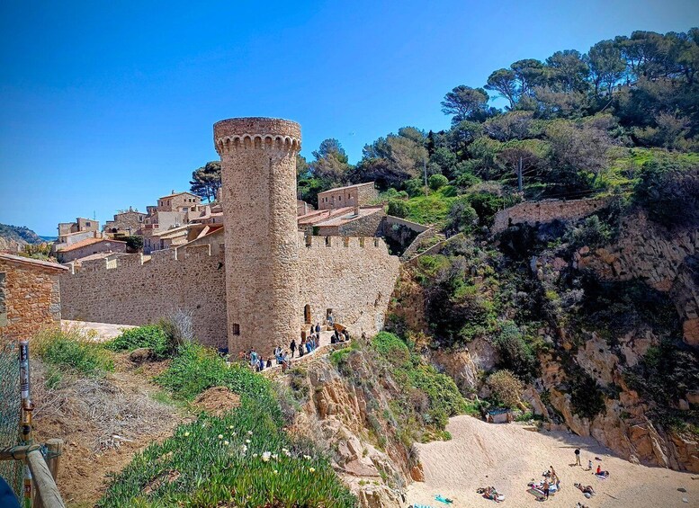 A historic stone fortress with a prominent tower, surrounded by lush greenery and a coastal landscape. 1