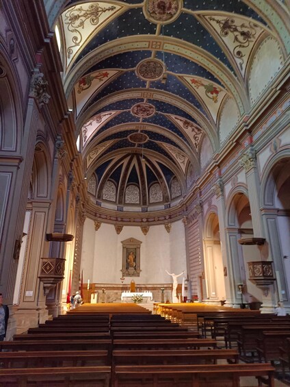 An ornate church interior with a high vaulted ceiling, detailed frescoes, and a central altar. 3