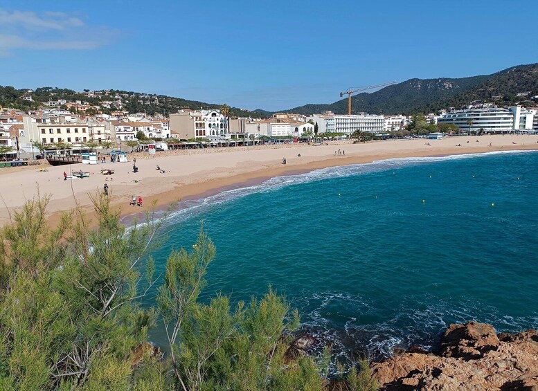 A coastal town with a sandy beach, clear blue sea, and buildings in the background. 5