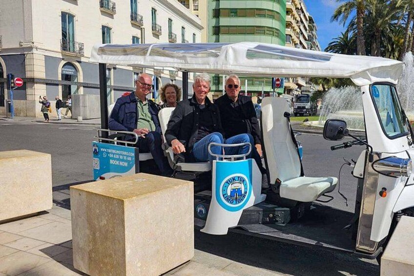 A golf cart with four passengers, a sign with a website URL, and a building in the background. 2