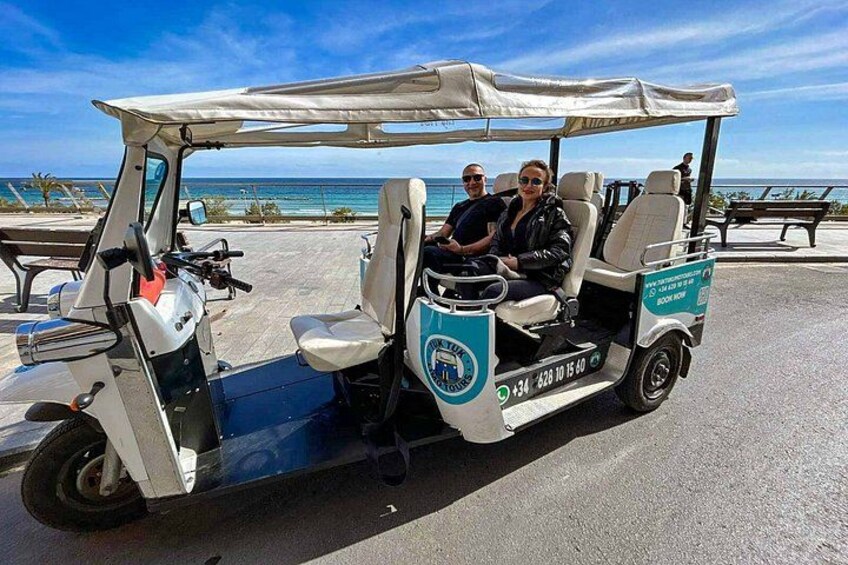 A golf cart with two passengers, a beach, and the ocean in the background. 3