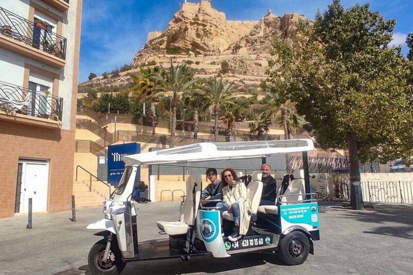 A three-seater electric vehicle parked on a street with a mountainous background. 3