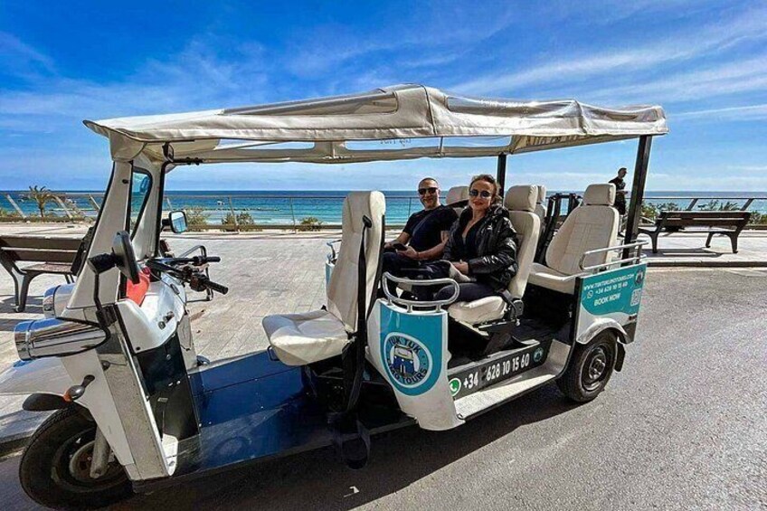 A golf cart with two people, a beach, and a clear sky. 1