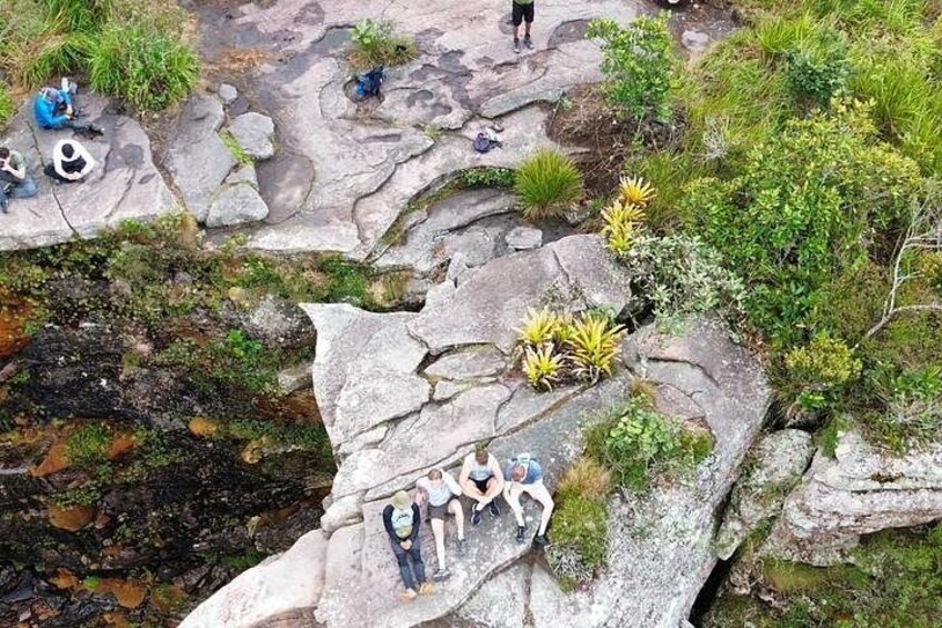 A rocky landscape with people sitting on the rocks, surrounded by greenery and small plants. 3