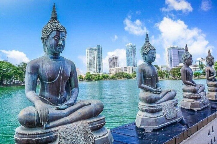 Une statue de Bouddha, assise, près d’un plan d’eau, avec une vue sur la ville en arrière-plan. 4