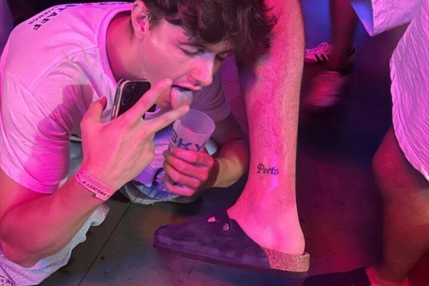A person in a pink shirt holding a drink and a phone, with a tattoo on their leg. 3