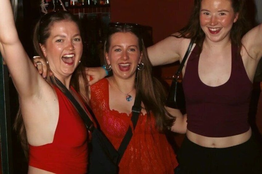 Three people standing close together, one in a red top, another in an orange top, and the third in a purple top. 2