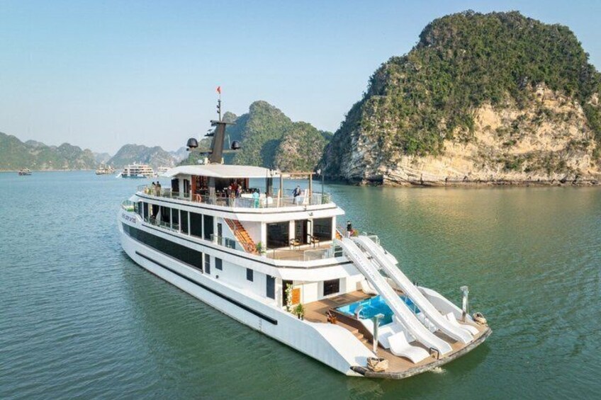 Ein weißes Boot mit Deck und Liegestühlen, an der steinigen Küste vertäut. 2