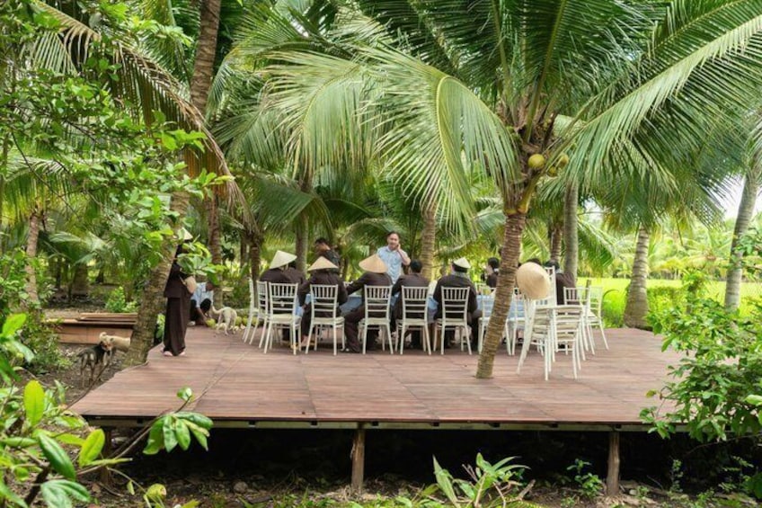 Une scène en bois, avec des chaises blanches disposées pour un événement, entourée de palmiers et de verdure. 3