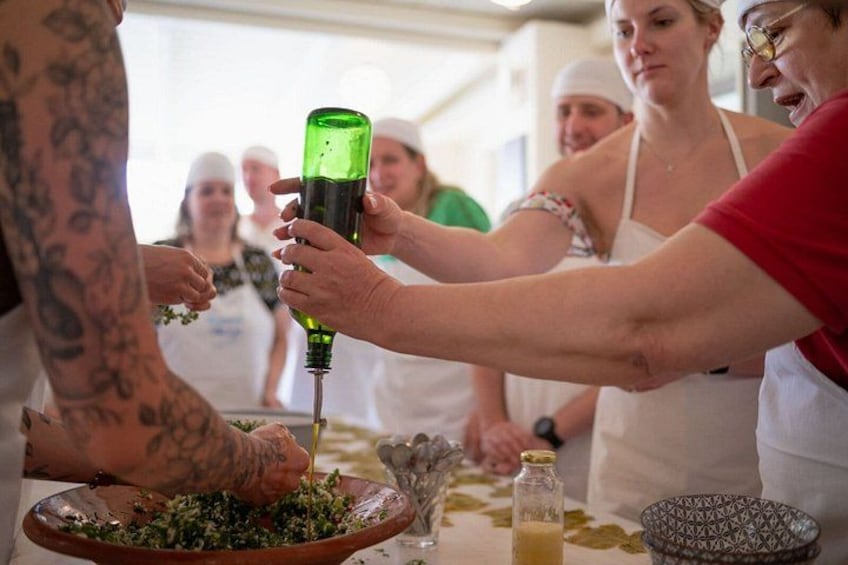 A group of people preparing food, with one person pouring a liquid from a green bottle into a bowl. 1