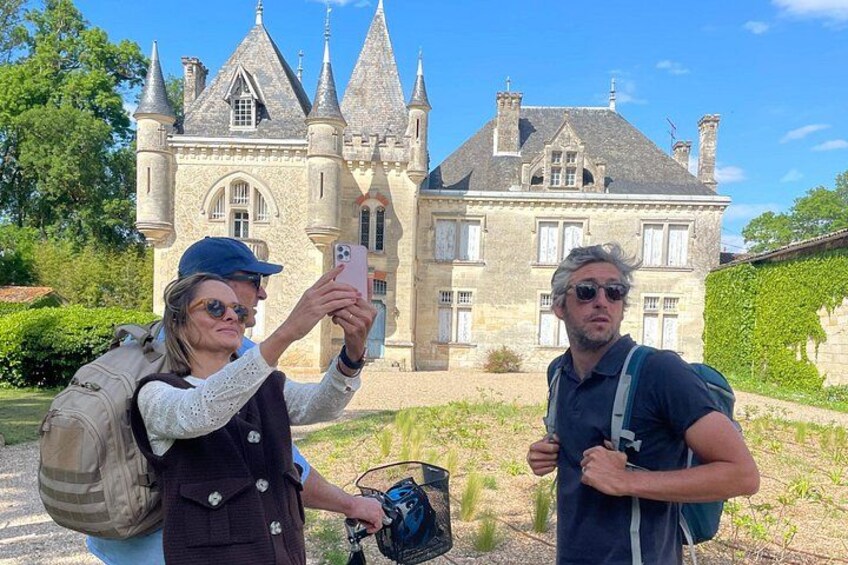 Two people taking a selfie in front of a historic building with a stone facade and pointed towers. 2