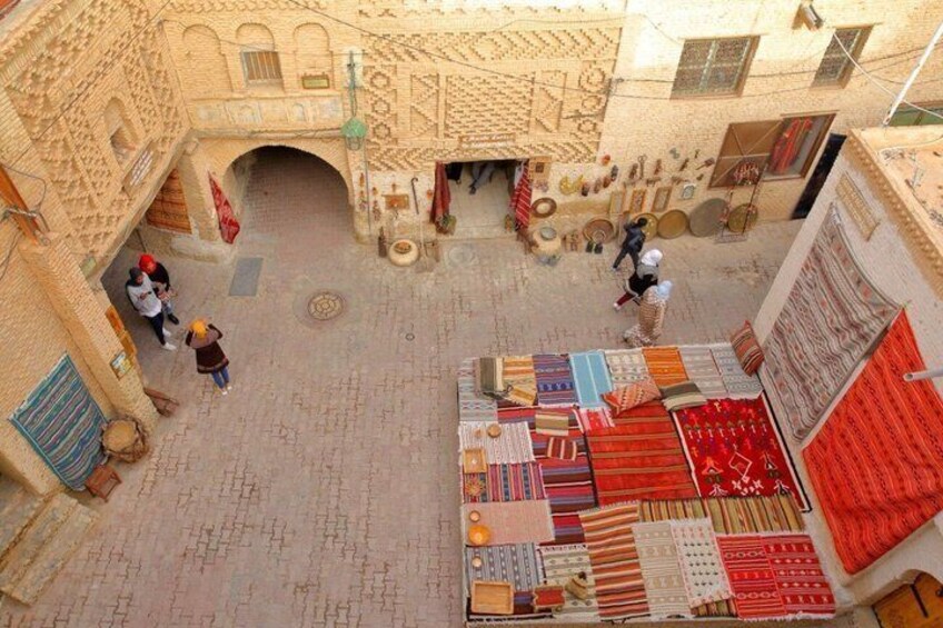 A courtyard with patterned architecture, a variety of textiles on display, and people walking. 3