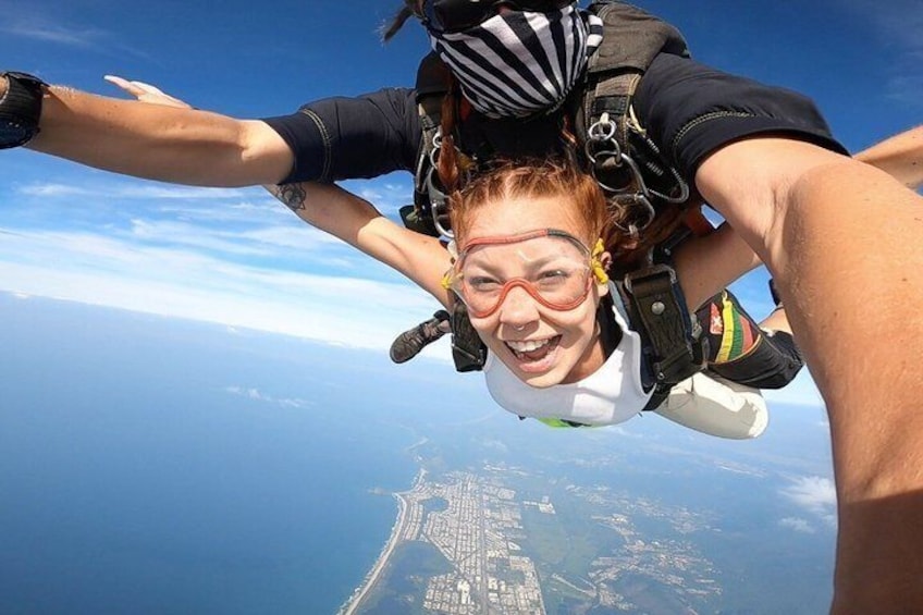 Eine Person mit Fallschirm springt aus einem Flugzeug, eine andere Person hält sie fest, darunter eine Küstenlinie. 2