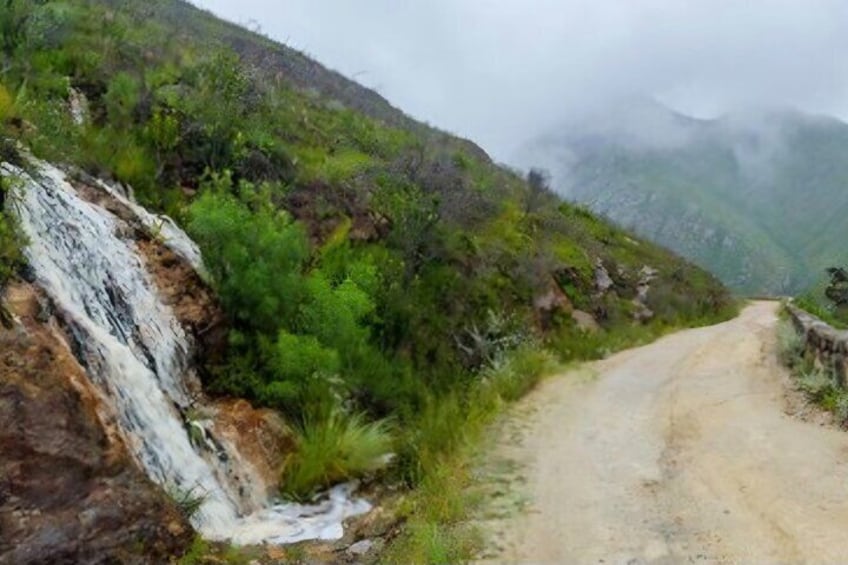 A dirt road leading through a mountainous area with a waterfall on the left. 3