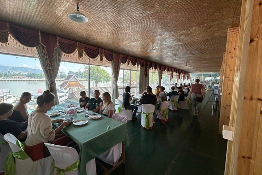 Un'area pranzo riparata, con tavoli e sedie, ampie finestre e vista su un corpo d'acqua. 3