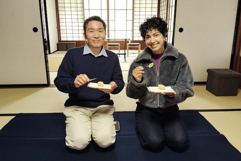 Deux personnes sont assises sur des tatamis dans une pièce de style japonais traditionnel, chacune tenant une petite assiette contenant de la nourriture. 2