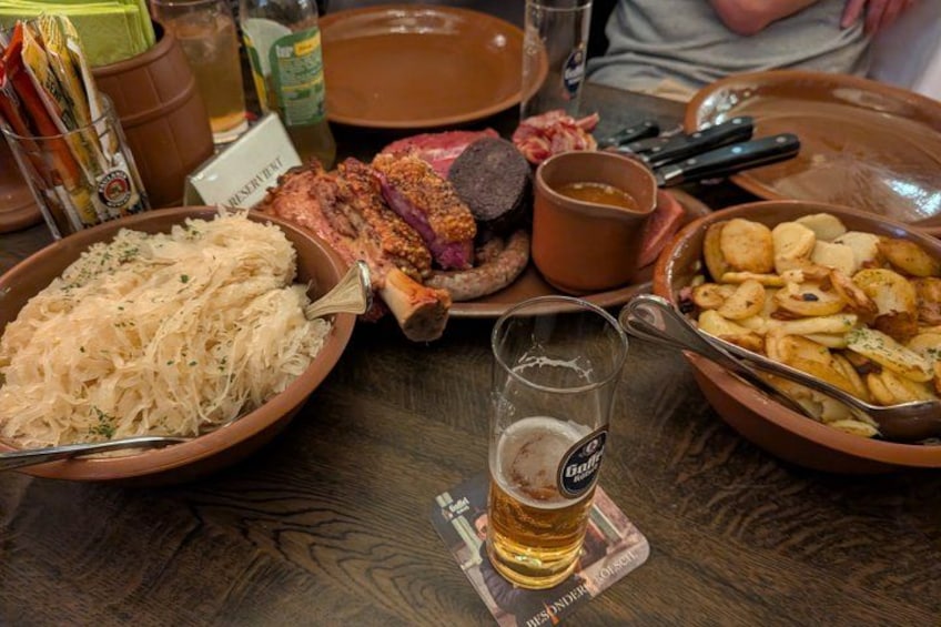 Un tavolo di legno con diversi piatti, un bicchiere di birra e una bottiglia di salsa. 2