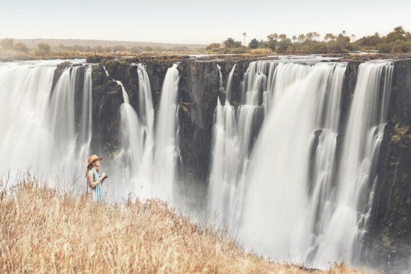 A waterfall with a person standing in the foreground. 1