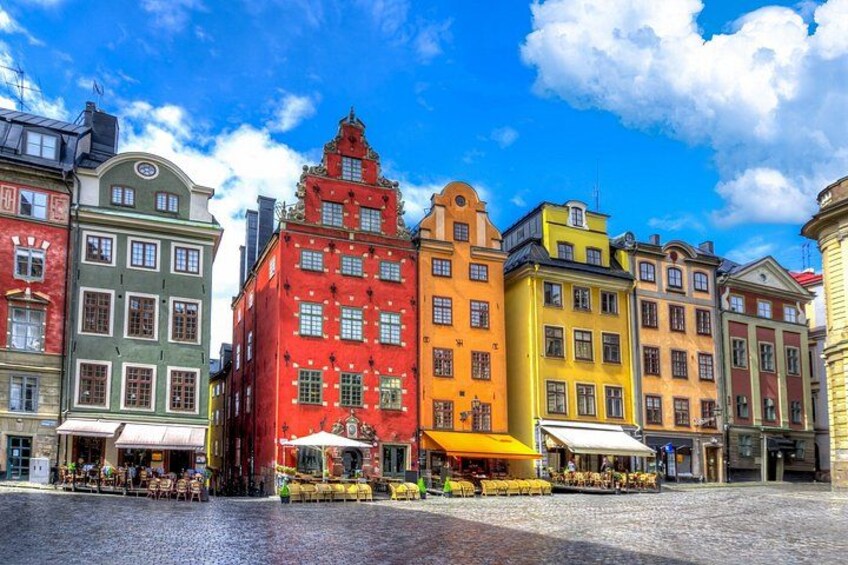 A cobblestone square with colorful historic buildings, outdoor cafes, and a clear blue sky. 3