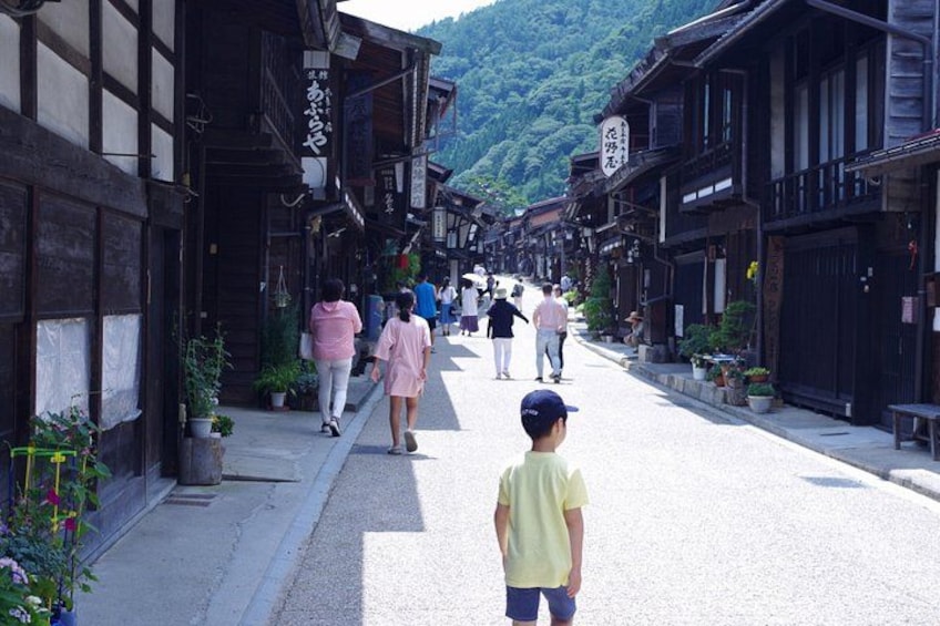 A traditional street with wooden buildings, pedestrians, and a child in the foreground. 5