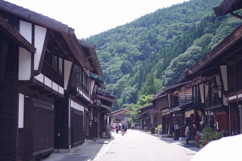 A traditional street lined with wooden buildings, a mountain in the background, and a few people walking. 4