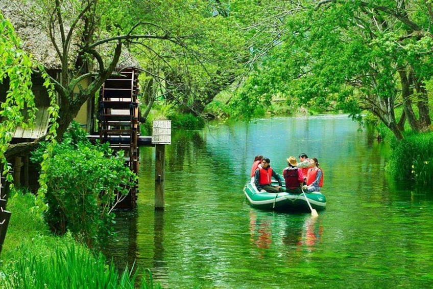 A river with a boat carrying people, surrounded by lush greenery and a wooden structure. 2