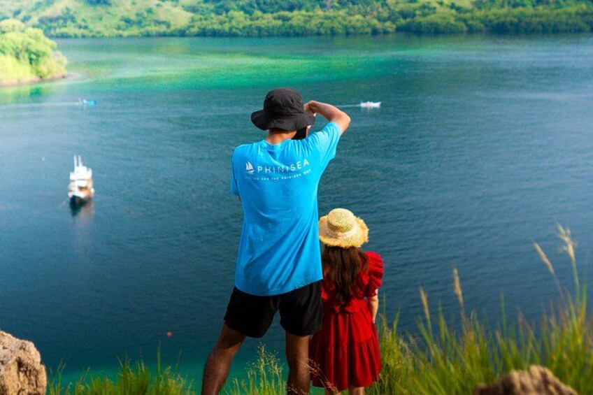 A person in a blue shirt and black shorts standing on a cliff overlooking a lake with a boat in the distance. 2