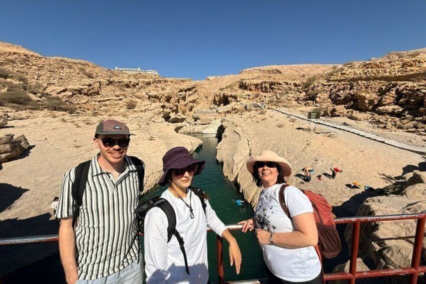 Three people standing by a rocky water channel with a bridge in the background. 3