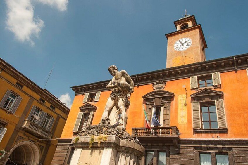 A building with a clock tower, a statue, and a flag. 2
