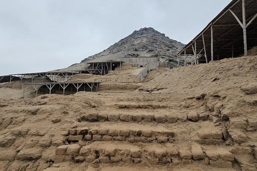 A desert landscape with a large rock formation, a metal structure, and a building with a roof. 5