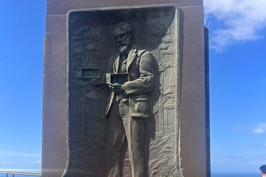 A bronze statue of a man holding a book and a magnifying glass, set in a niche with a clear blue sky in the background. 4